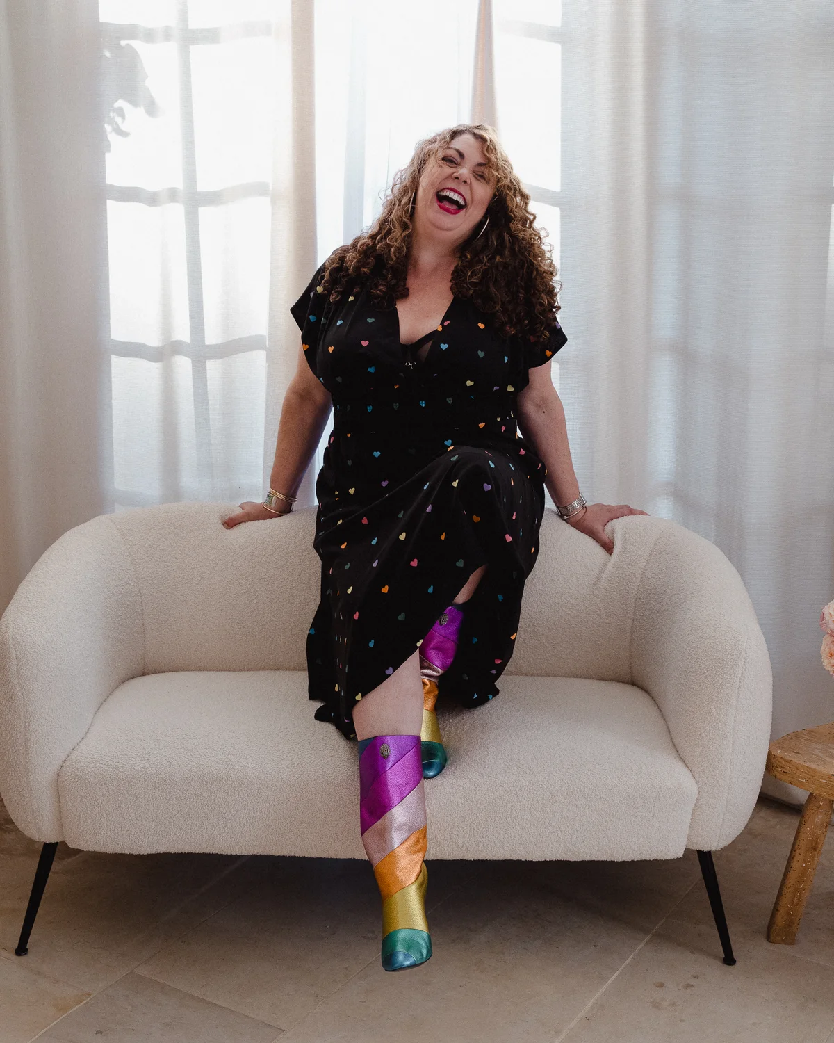 Carine Soriano éclate de rire sur un canapé, bottes arc-en-ciel